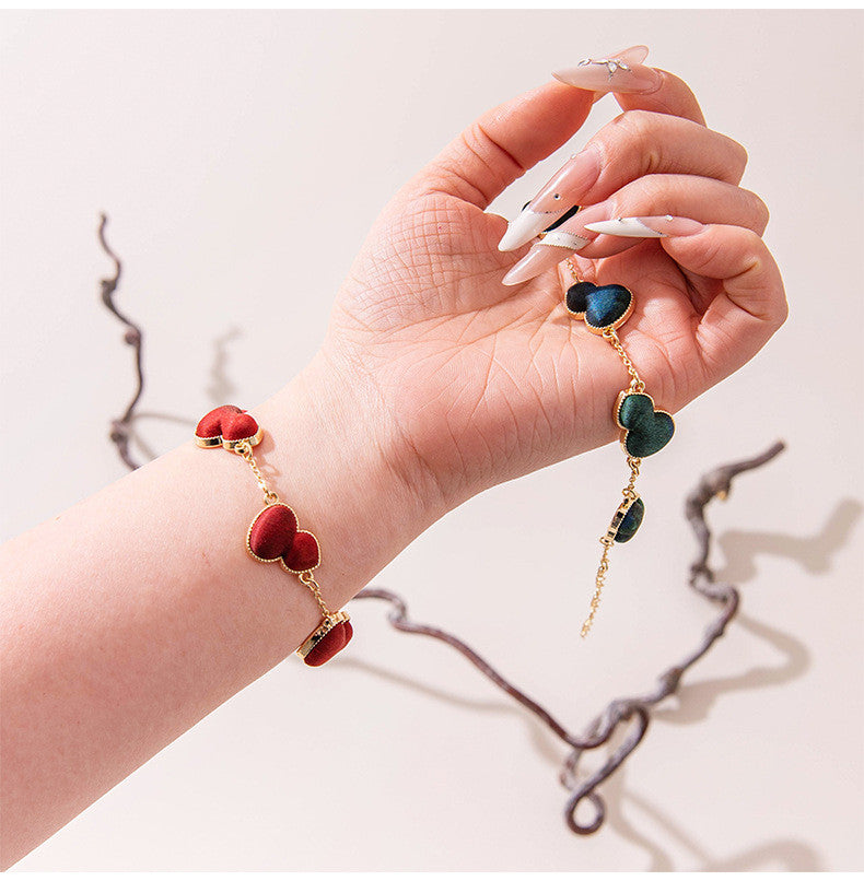 Xiangyunsha silk four-leaf clover bracelet in crimson-teal mix held in hand