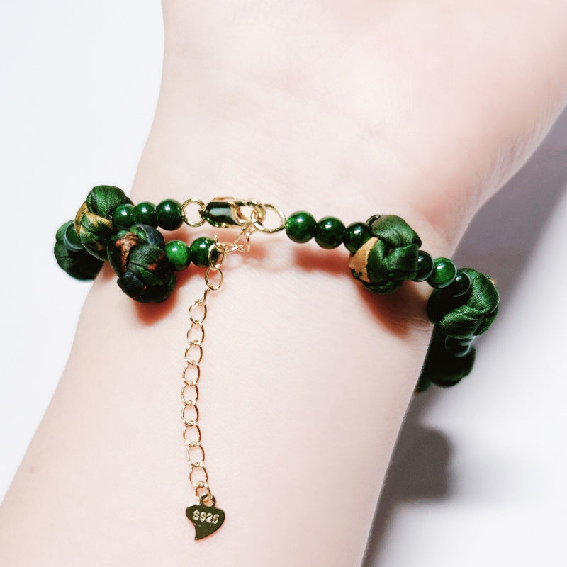 Xiangyunsha silk rose knot bracelet in forest green worn on wrist, close-up